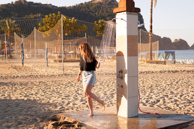 Une fille en short et un t-shirt noir sur la plage près de la douche