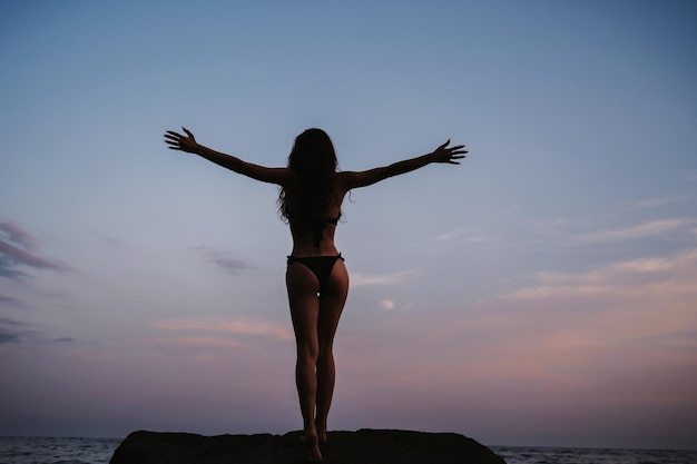 Fille silhouette avec un butin sexy debout sur les rochers sur la plage au bord de la mer