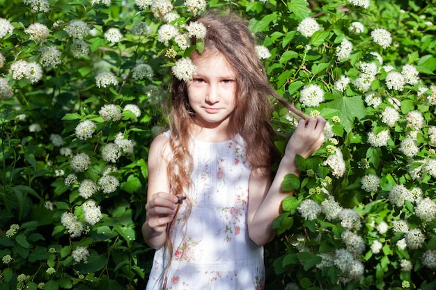 Une fille de six ans aux cheveux longs dans un arbuste à fleurs