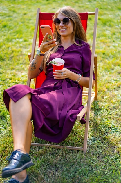 fille avec un smartphone et un cocktail sur la nature dans une chaise longue. Jour de congé d'été.