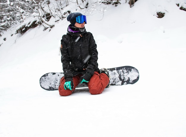 Une fille avec un snowboard est assise sur le flanc de la montagne