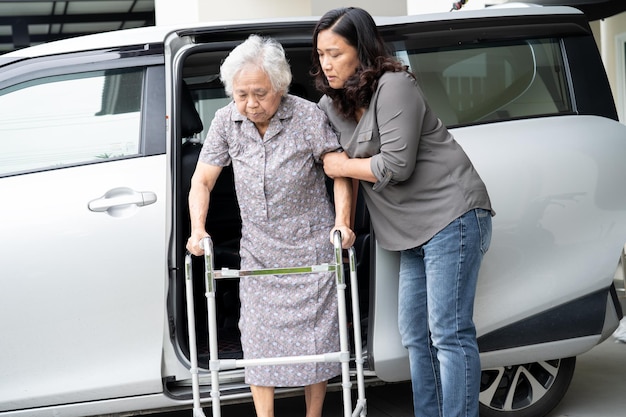 La fille soignante aide et soutient une patiente asiatique âgée ou âgée qui se prépare à sortir de sa voiture.