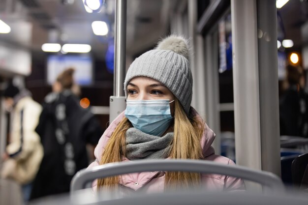 Une fille solitaire dans un masque facial monte un tram la nuit en période de pandémie