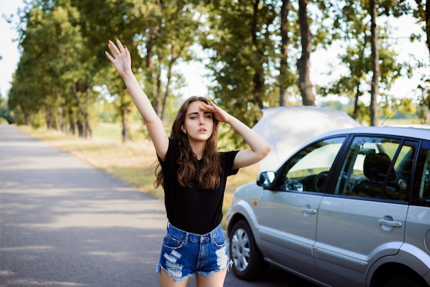 Fille solitaire se tient près d'une voiture cassée et arrête les passants pour demander de l'aide