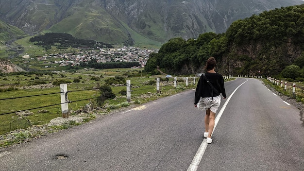 Une fille solitaire va sur la route du village devant les montagnes