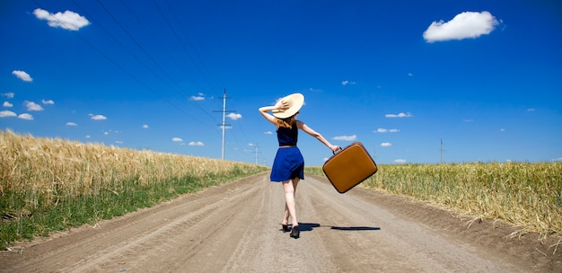 Fille solitaire avec valise à route de campagne.