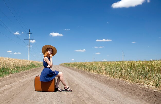 Fille solitaire avec valise à route de campagne.