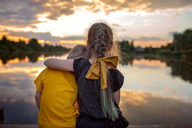 Fille avec son jeune frère regardant le magnifique coucher de soleil sur le lac lifestyle voyage en famille vue arrière