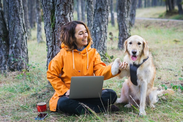 Fille avec son ordinateur et son chien à l'extérieur