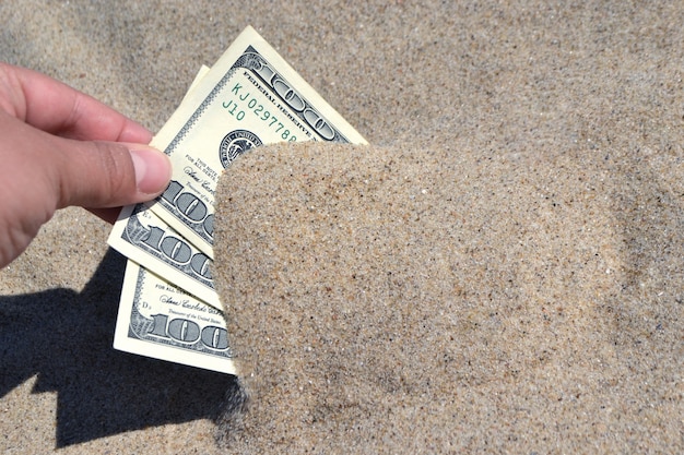 Une fille sort du sable des billets de trois cents dollars.