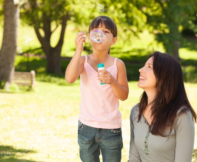 Fille soufflant des bulles avec sa mère dans le parc