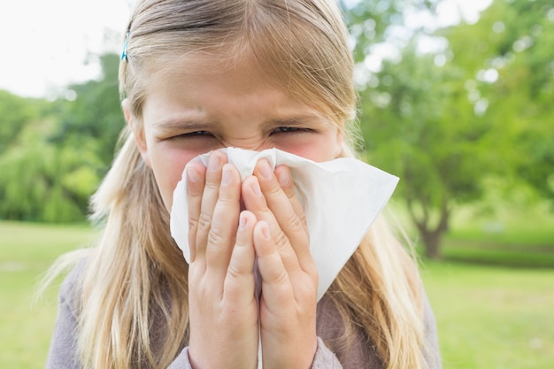 Fille soufflant le nez avec du papier de soie au parc
