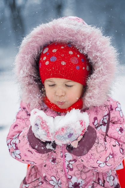 La fille souffle sur la neige dans les mains