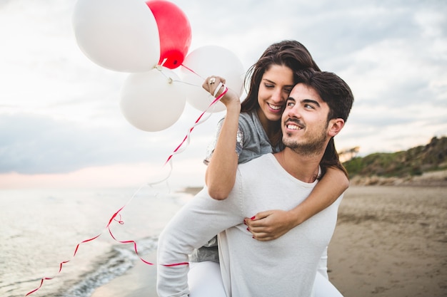 Fille souriante avec des ballons tandis que son petit ami lui porte sur son dos