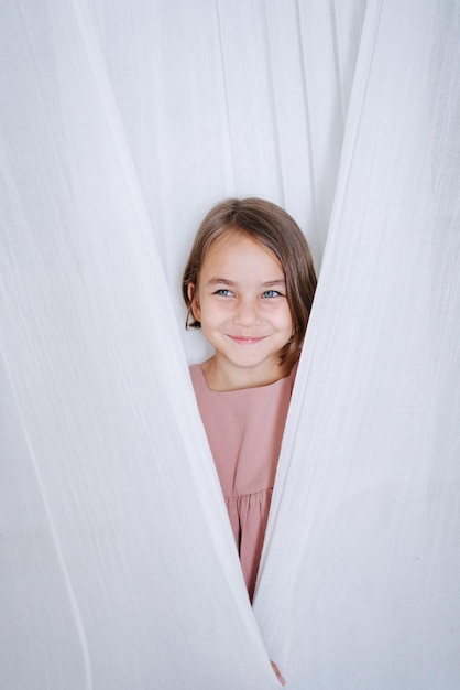 Photo fille souriante cachée derrière des rideaux dans une robe beige