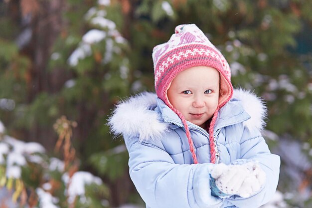 Une fille souriante dans un chapeau rose et une veste bleue avec fourrure. En hiver, il tient de la neige dans ses mains. Regarde la caméra. Place pour le texte, la bannière, le nouvel an, Noël