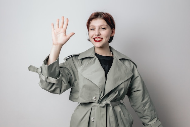 Une fille souriante dans un manteau vert à la mode montre la paume de sa main