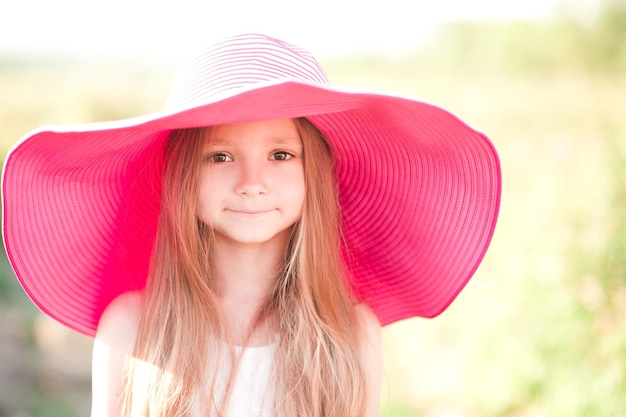 Fille souriante drôle d'enfant utilisant le grand chapeau rose dehors