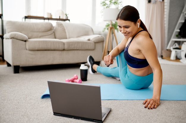 Fille souriante est assise sur le sol à la maison, formation en ligne sur l'ordinateur portable