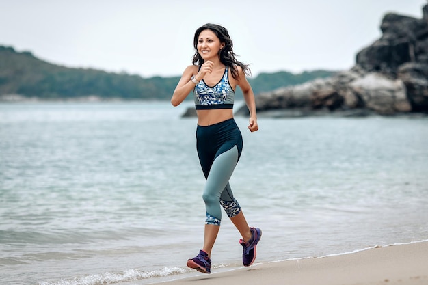 Une fille souriante en forme court sur la plage de sable de la mer d'Andaman, concept de bien-être