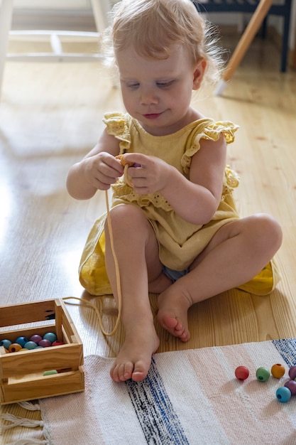 Fille souriante jouant des perles amovibles en bois pour le développement de la motricité fine maria montessori ma...