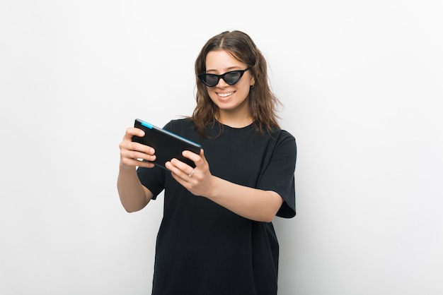 Une fille souriante joue sur sa tablette sur fond blanc.