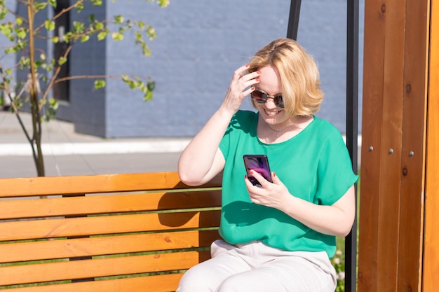 Une fille souriante à lunettes de soleil tenant un smartphone dans ses mains en tapant du texte à des amis qui prennent rendez-vous