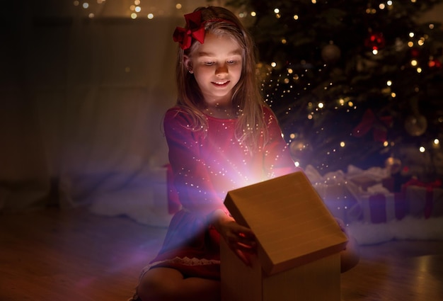 Une fille souriante ouvre un cadeau de Noël la nuit.