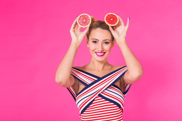 Fille souriante avec pamplemousse coupé en deux fruits à la main sur un mur rose