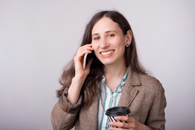 Fille souriante parle au téléphone et tasse à emporter sur blanc