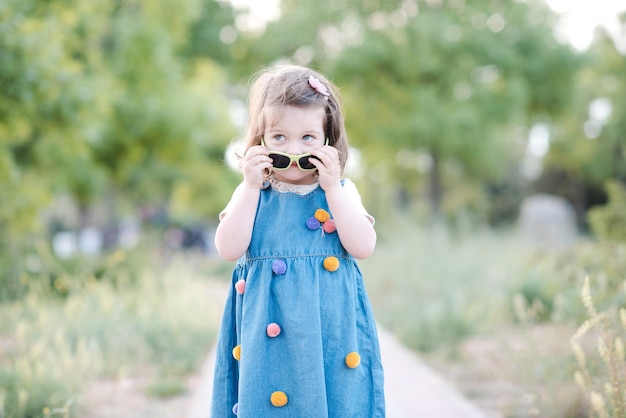 Fille souriante portant des lunettes de soleil et une robe en jean à l'extérieur