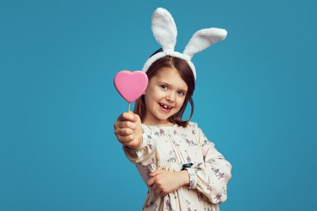 Fille souriante et tenant un cookie en forme de coeur portant des oreilles de lapin