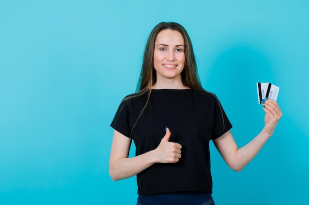 Une fille souriante tient des cartes de crédit et fait un geste parfait sur fond bleu