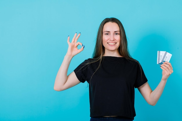 Une fille souriante tient des cartes de crédit et montre un geste correct sur fond bleu