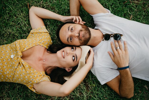 Une fille souriante vêtue d'une robe et d'un chapeau est allongée près de son petit ami avec une barbe sur l'herbe dans le parc de Valence. Un couple de touristes profite de l'été en Espagne.