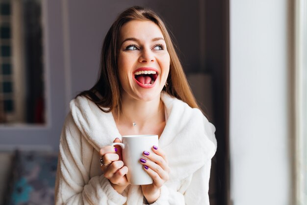 Une fille avec un sourire émotionnel tenant une tasse de thé ou de café.