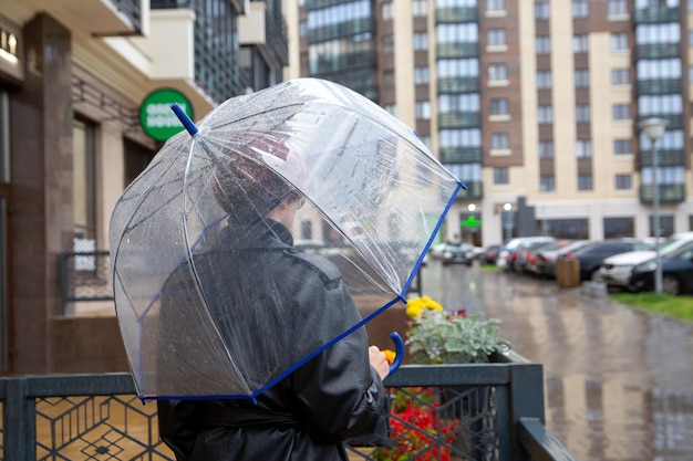 Une fille sous un parapluie transparent se tient sous la pluie dans une rue de la ville.