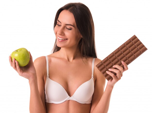 Fille en soutien-gorge blanc tient une pomme et une barre de chocolat.