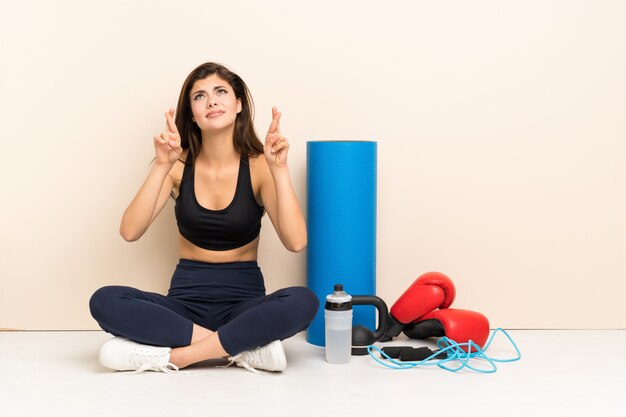 Fille de sport adolescent assis sur le sol avec les doigts qui se croisent et souhaitant le meilleur