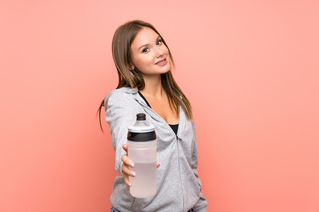 Fille de sport adolescent avec une bouteille d'eau sur fond rose isolé