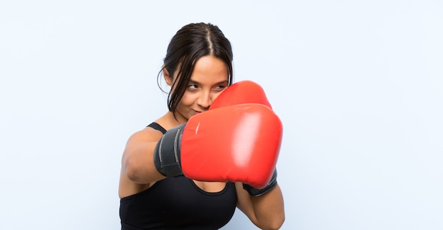 Fille de sport jeune avec des gants de boxe sur mur bleu isolé