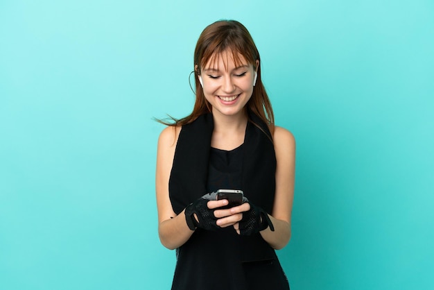 Fille de sport rousse isolée sur fond bleu envoyant un message avec le mobile