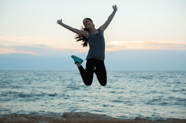 Fille de sport sautant sur la plage au coucher du soleil