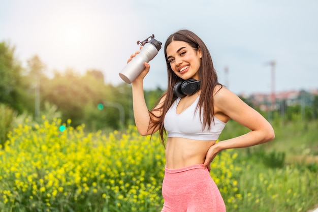 Fille De Sport Urbain Avec Des écouteurs De L'eau Potable Dans La Formation Au Coucher Du Soleil, Les Devoirs