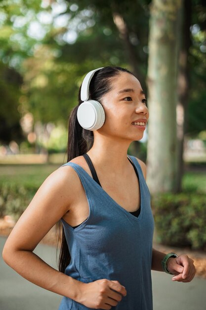 Fille sportive asiatique courant dans le parc pendant qu'elle écoute de la musique sur des écouteurs sans fil