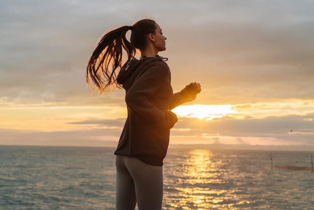 Une fille sportive aux cheveux longs va courir à la mer au coucher du soleil veut perdre du poids