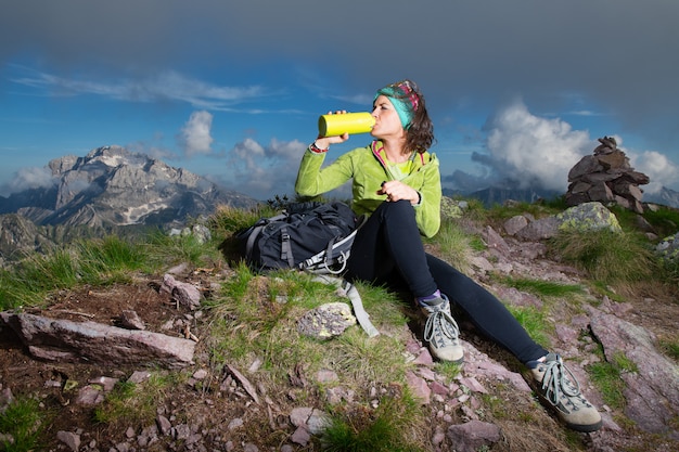 Une fille sportive boit à la bouteille d'eau après avoir conquis le sommet d'une montagne