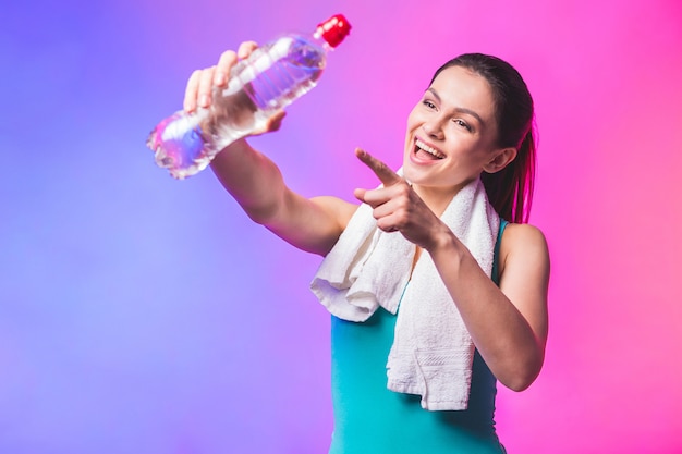 Fille sportive avec une bouteille d'eau et une serviette sur ses épaules. Photo du modèle de fitness isolé sur fond blanc.
