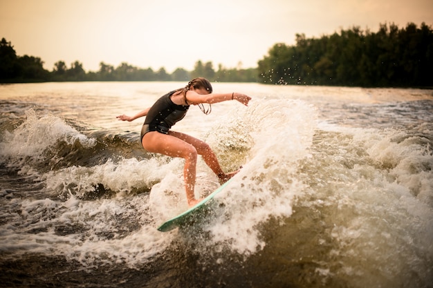 Fille sportive faisant un tour sur le wakeboard sur la rivière au coucher du soleil