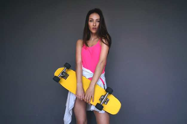 Fille sportive en maillot de bain bikini rose tient son longboard jaune